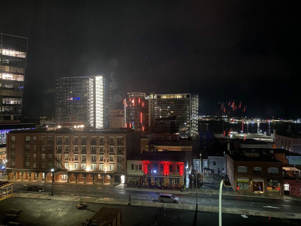 Halifax at night - view from hotel room. Empty building lot/parking lot in foreground, bars and restaurants lit up and tower block with harbour behind. 