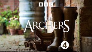 BBC The Archers graphic of wellington boots next to a house with a water butt and plants in terracotta pots in the background.