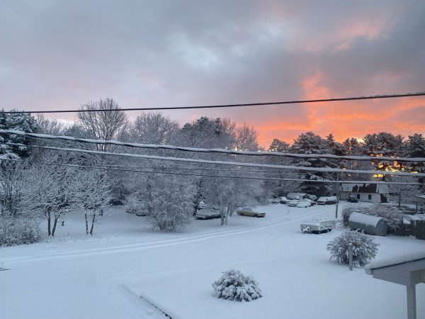 View from an upper floor window. power lines across the middle of the photo and a red sunrise over a snowy scene with cars and front yards